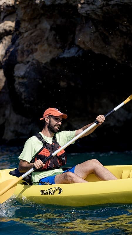 Kayaker entering a sea cave with their open kayak along the coast of Els Colls-Miralpeix.