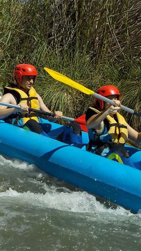 Pair paddling in coordination on an inflatable canoaraft overcoming a rapid on the Cabriel River.