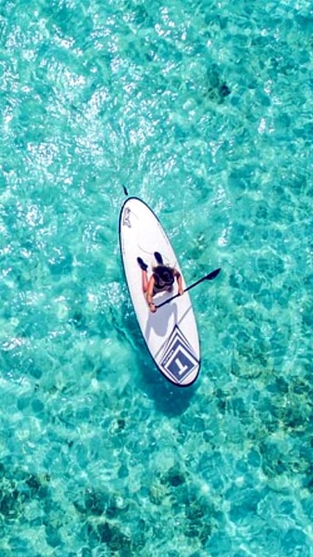 Group of people practicing paddle surf in the turquoise waters of Menorca's north coast near a cliff.