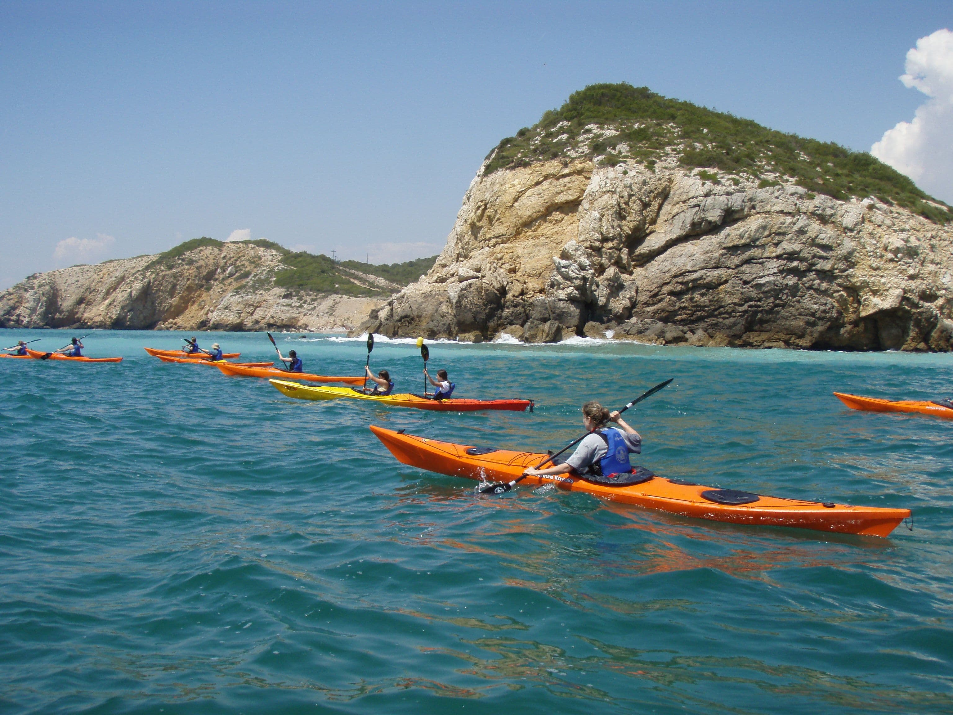 Group of kayakers paddling along the vertical walls of the Garraf cliffs from the sea.